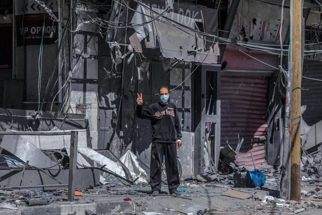 Un hombre palestino hace la señal de la victoria junto a un edificio en ruinas bombardeado por Israel, el pasado martes.