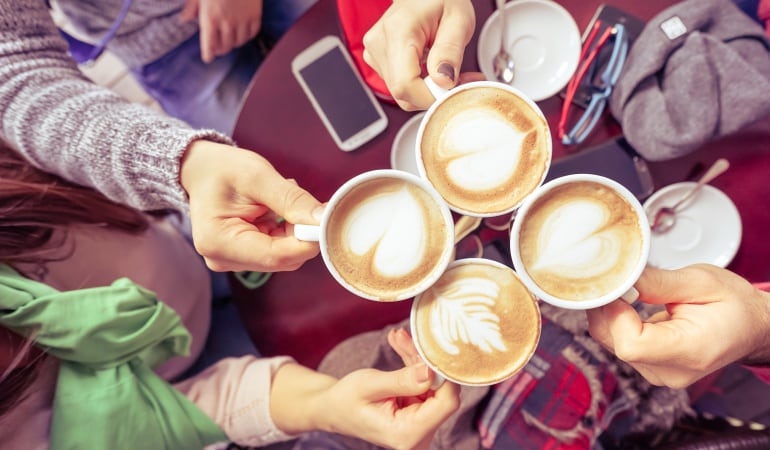 Imagen de varias personas brindando con cafés.