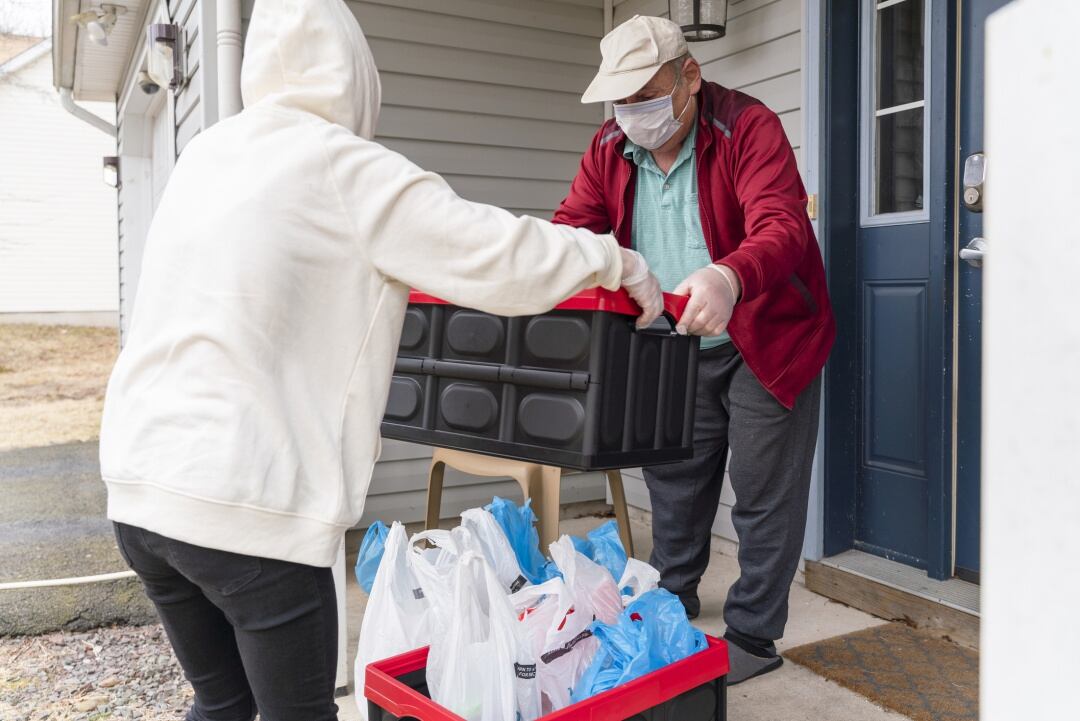 Una joven entrega los comestibles embalados en contenedores de plástico reutilizables a un cliente, un hombre de la tercera edad, en el porche de su casa durante el brote de COVID-19