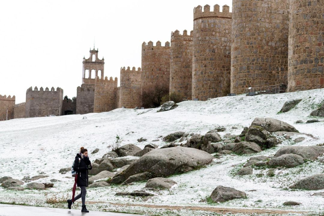 Una mujer camina junto al lienzo norte de la muralla de Ávila cubierta por una fina capa nieve caída en las últimas horas.