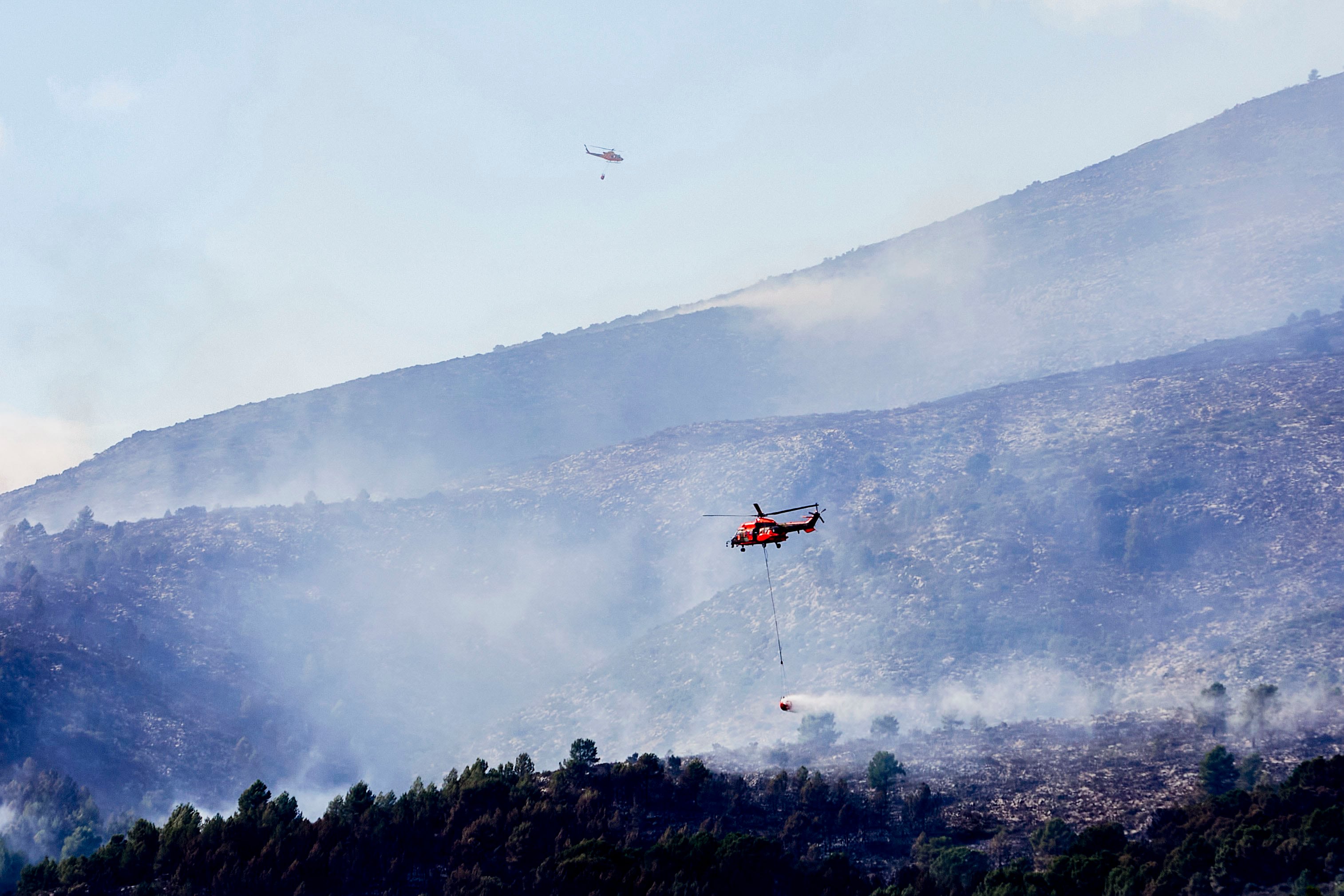 El humo generado por el incendio, que ha cubierto la zona, y las fuertes rachas de viento han complicado los trabajos de extinción de los medios aéreos. EFE/ Natxo Francés