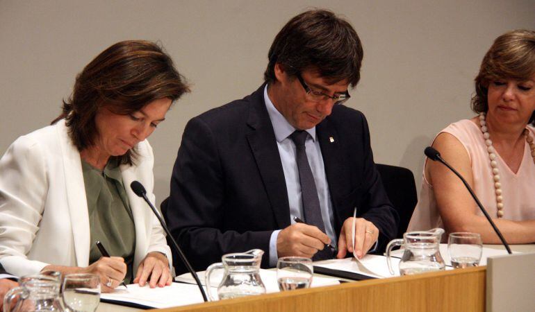 El president de la Generalitat, Carles Puigdemont, i la directora de BBVA Espanya, Cristina de Paria, signen el conveni, amb la consellera de Governació i Habitatge, Meritxell Borràs.