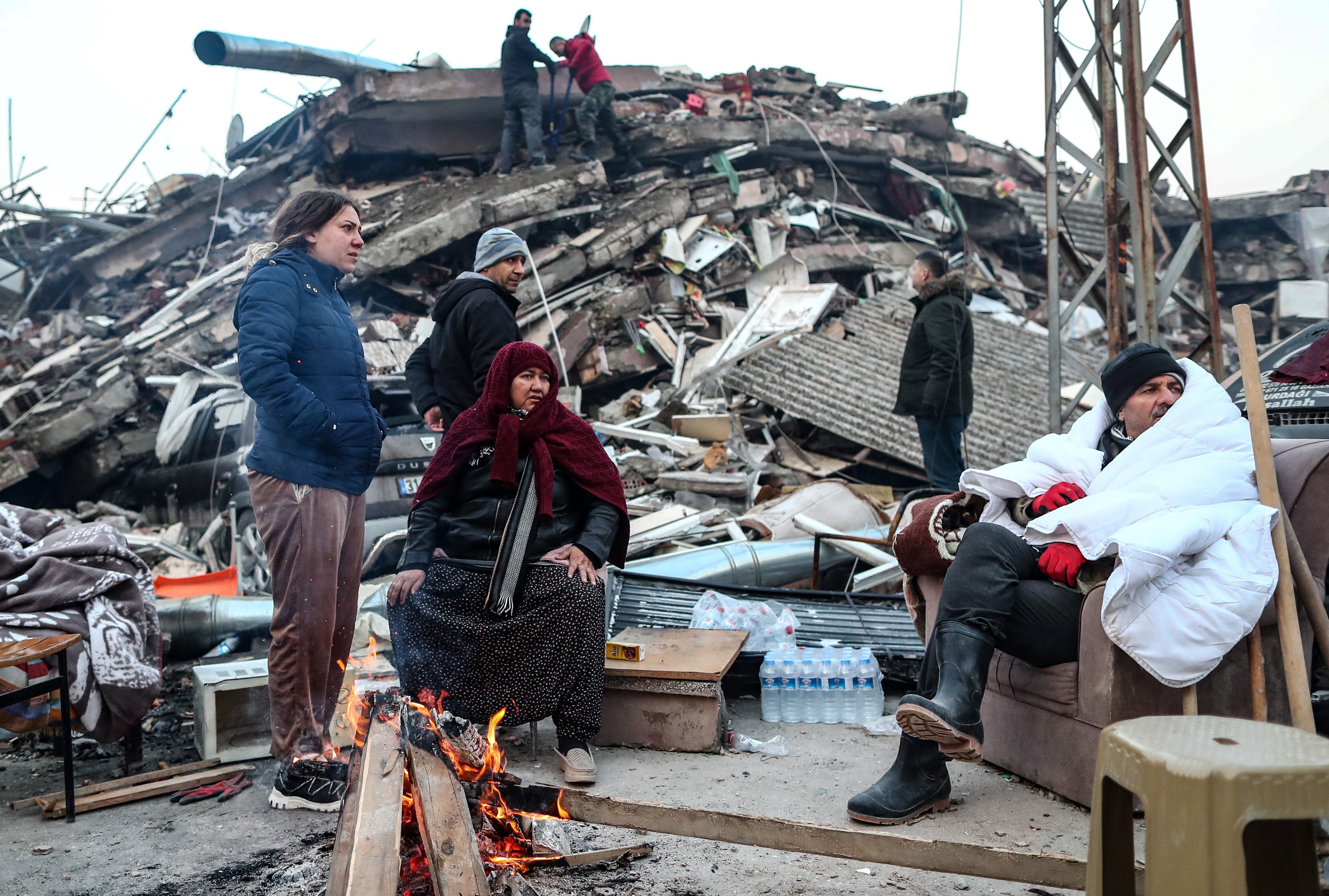 La gente se calienta cerca de los edificios derrumbados tras un gran terremoto en Hatay