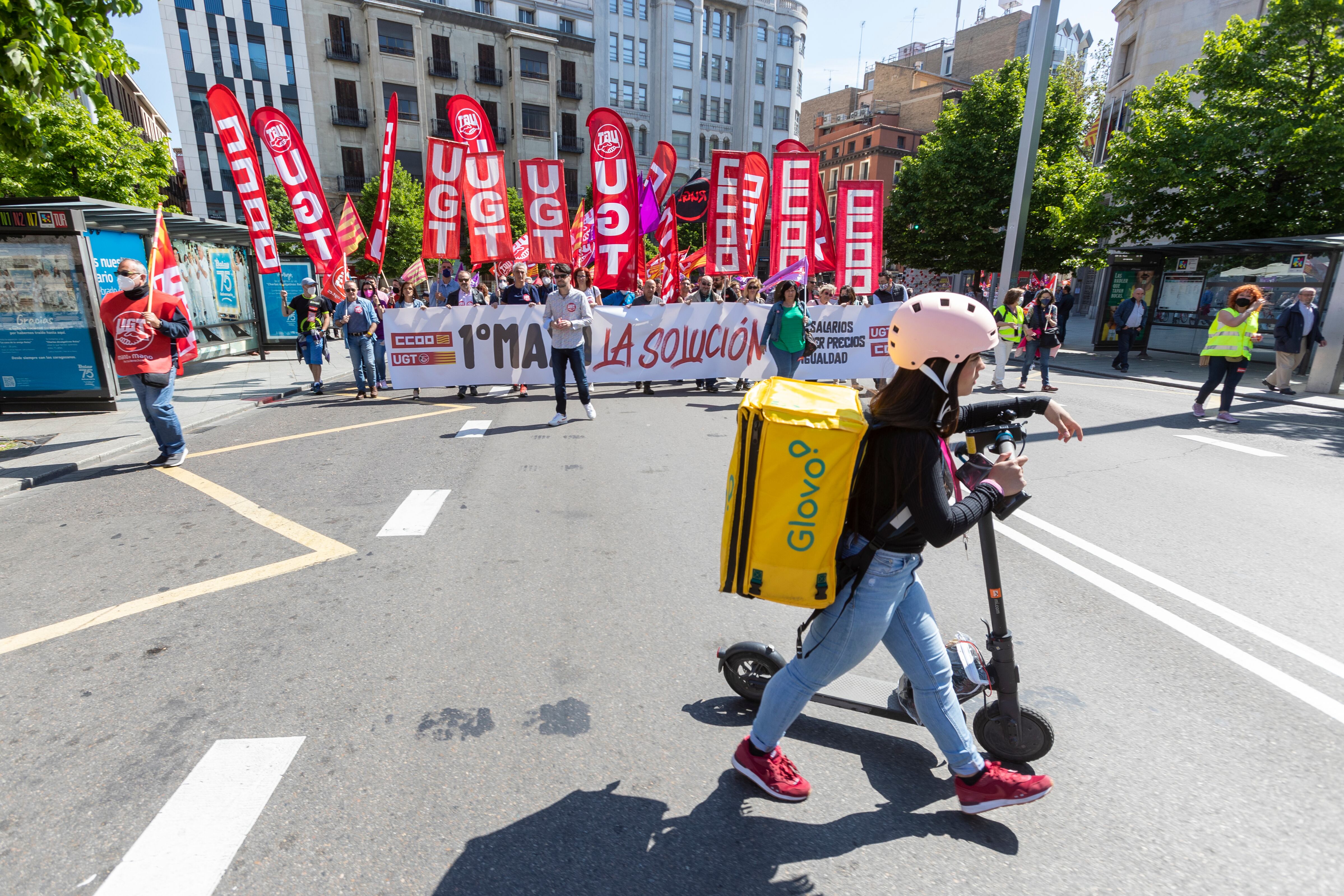 Una rider mensajera pasa por delante de la cabecera de la manifestación de UGT y CCOO del Primero de Mayo en Zaragoza. EFE/ Javier Belver