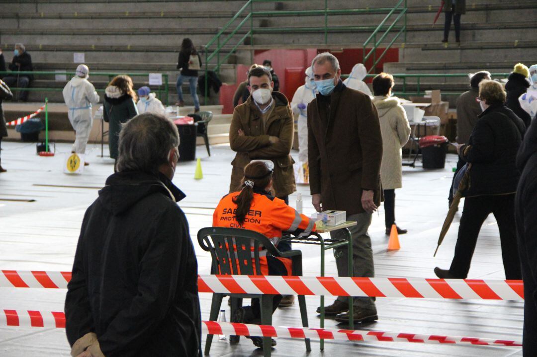 El alcalde de Cuéllar conversa con un voluntario de Protección Civil acompañado del delegado territorial durante  la segunda jornada de cribado en el pabellón de la villa