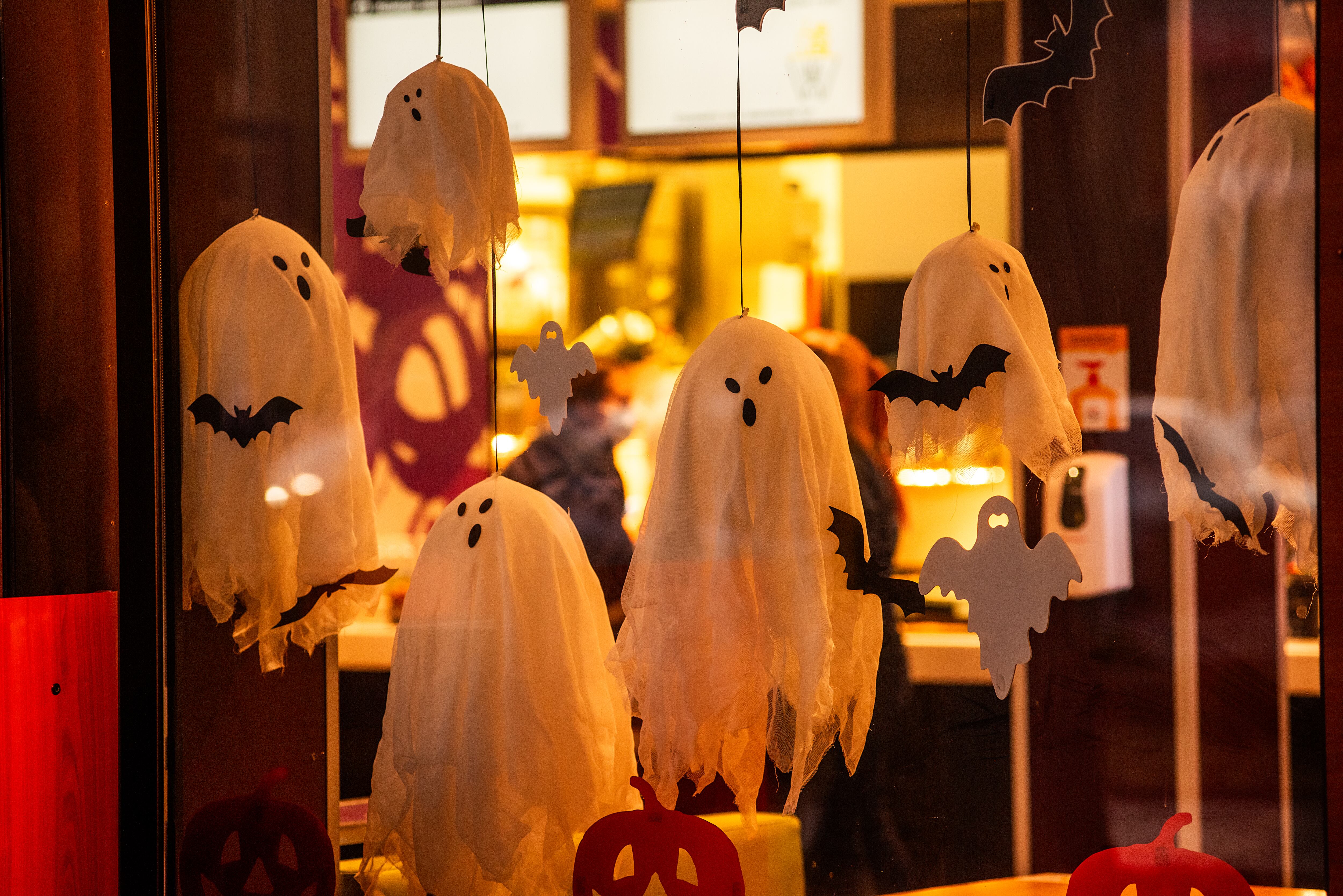 Bright, spooky city store decorated for Halloween. Street decoration. Scary ghosts hanging outside the window, black bats sitting on spider webs, stickers in shape of orange pumpkins. Festive interior