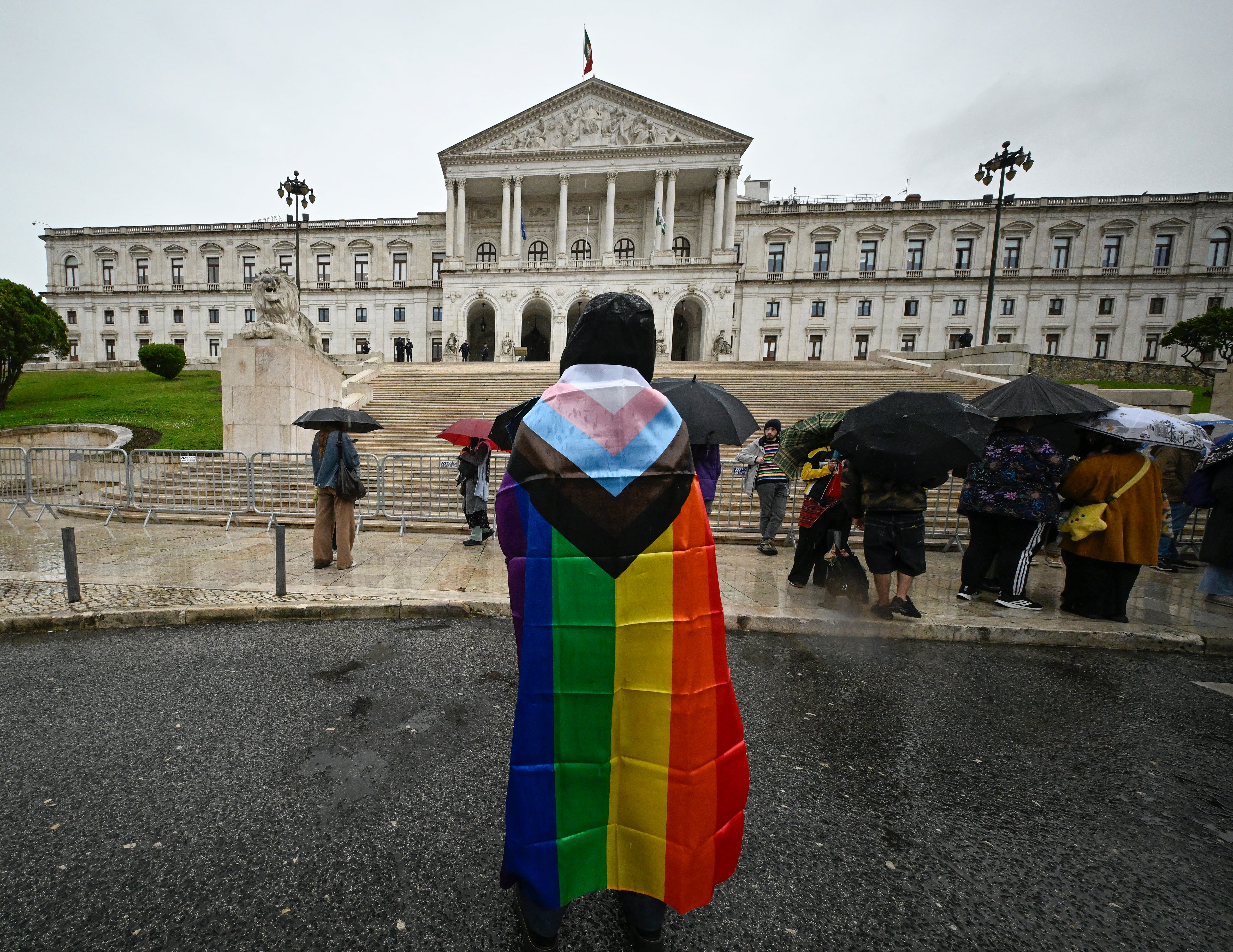 Una persona con una bandera LGBTQIA+, frente al Parlamento portugués en marzo de 2026