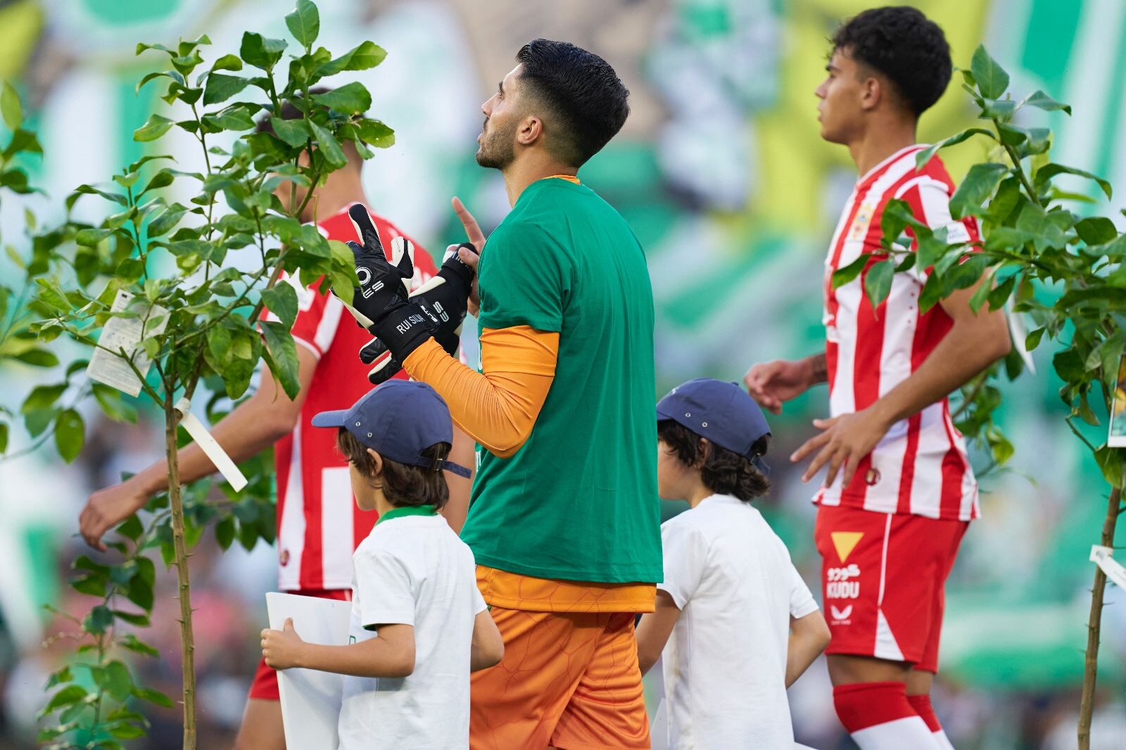 Niños y futbolistas del partido Betis -Almería Forever Green saliendo entre árboles y niños con fotografías alusivas al medioambiente