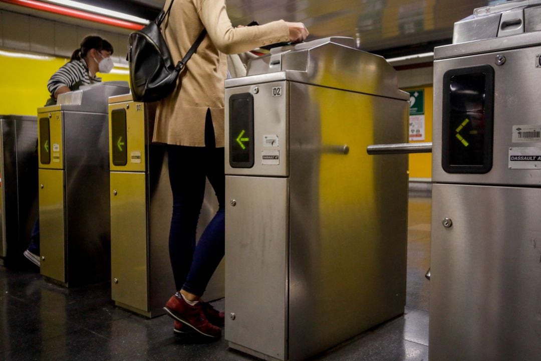 Dos personas pasan los tornos de entrada del metro de Ciudad Lineal, Madrid 