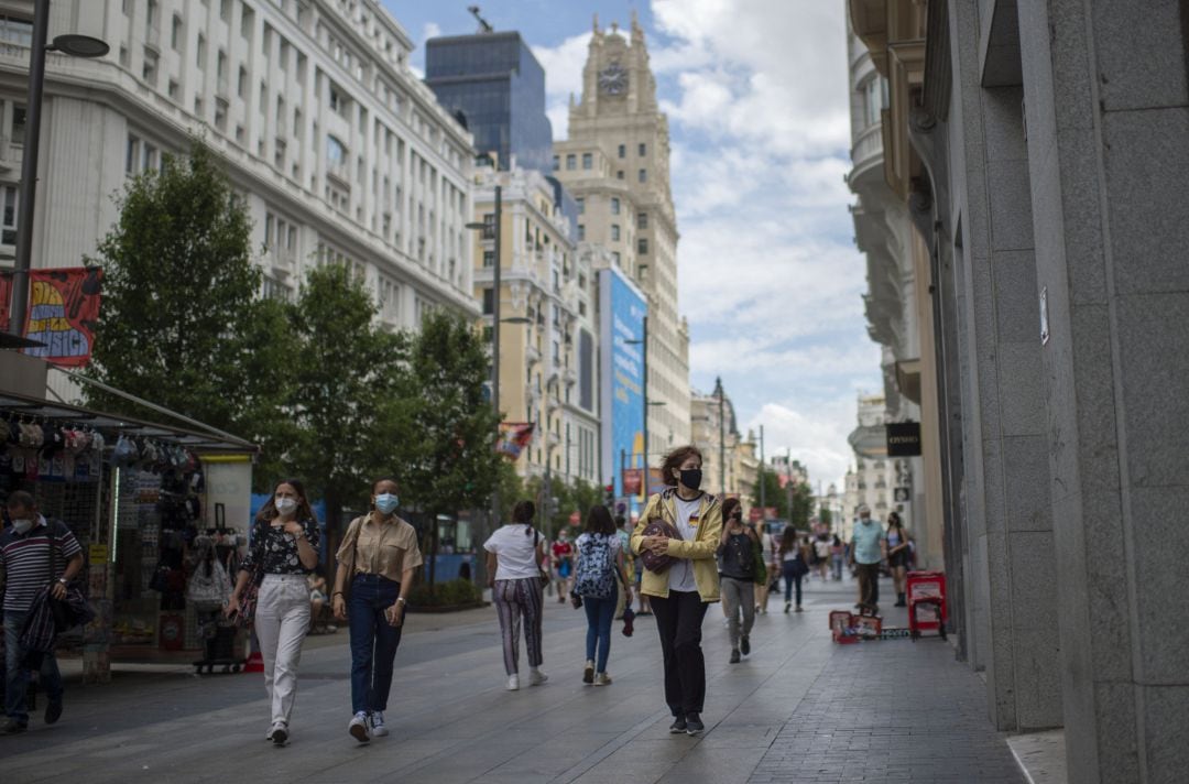 Varias personas caminan por la Gran Vía de Madrid con mascarilla.