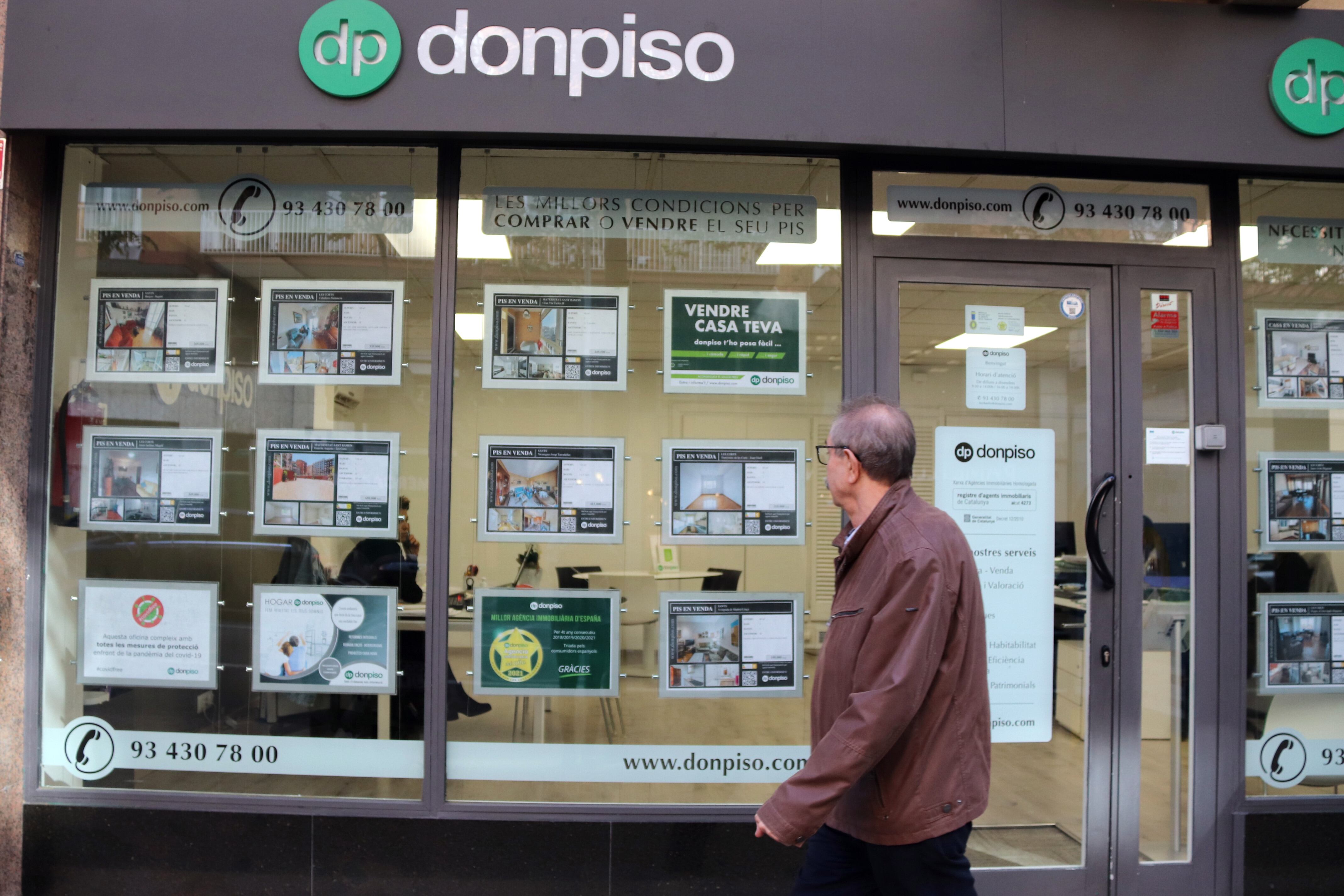 Un home passa per davant dels cartells que anuncien els pisos a la venda en la immobiliària "donpiso"