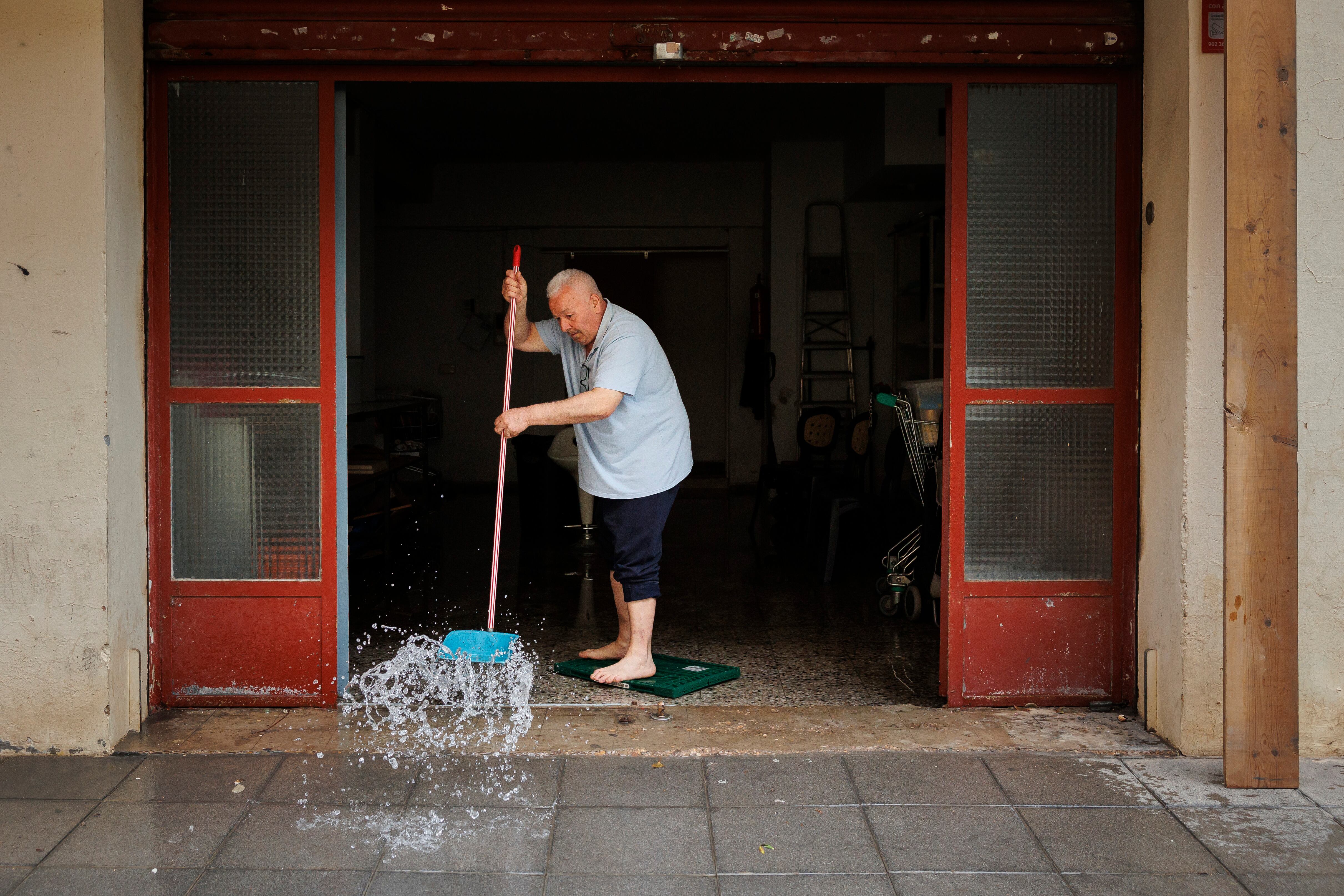 Una persona achica agua de un local comercial de Valencia tras las fuertes lluvias del martes 3 de mayo