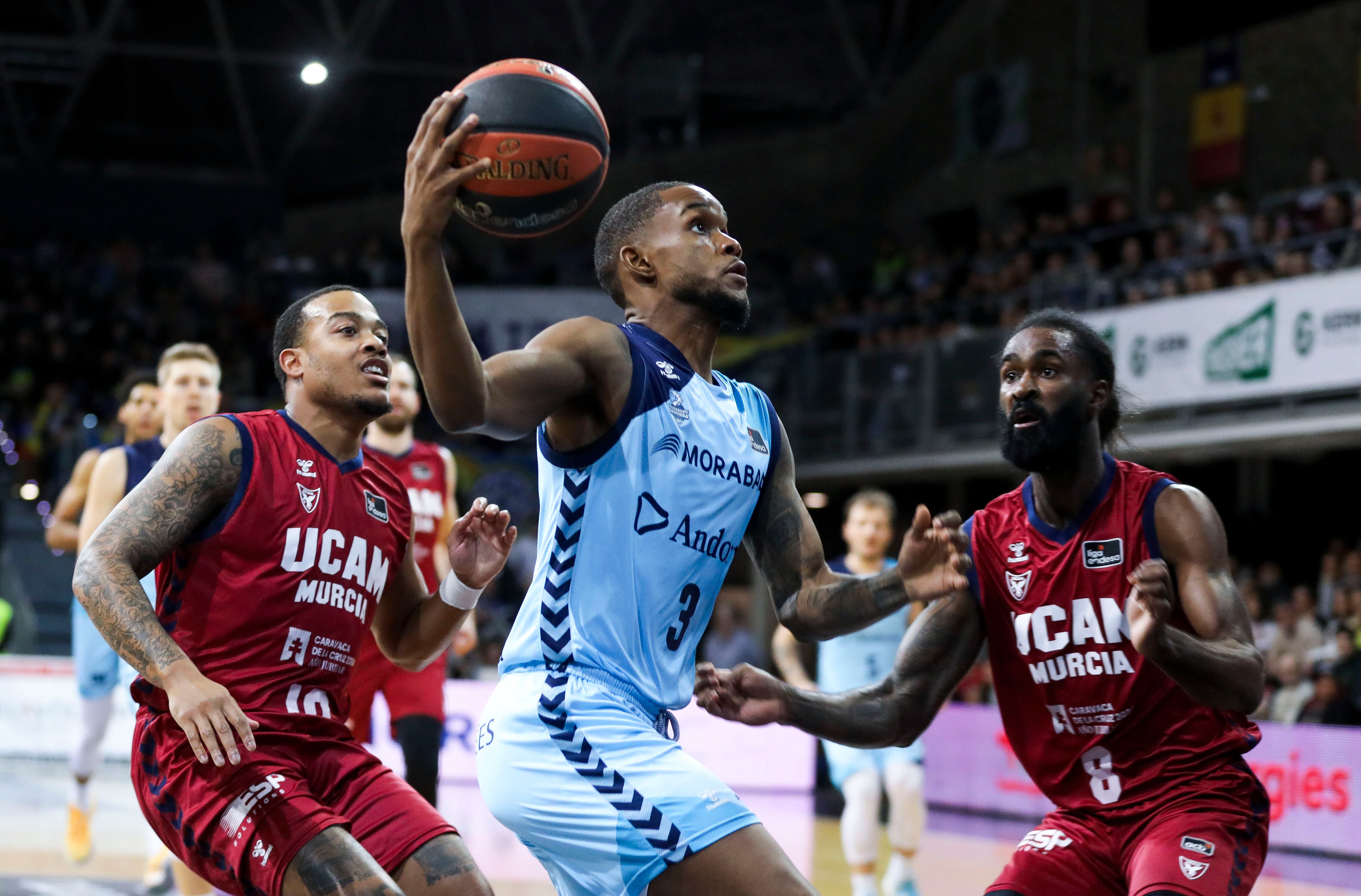 Jean Montero (c) condueix la pilota davant Troy Caupain (i), i Howard Sant-Roos (d), de l'UCAM Múrcia, aquest dissabte durant el partit de la 17a jornada de la Lliga Endesa de bàsquet, al Polisportiu d'Andorra.