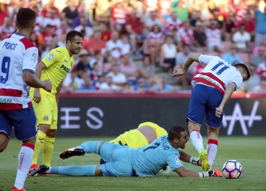 El portero del Villarreal Asenjo intenta parar un balón ante el defensa Mario Gaspar y los jugadores del Granada durante el partido correspondiente a la primera jornada de Liga que ambos equipos disputan en el estadio de Los Cármenes, en Granada.