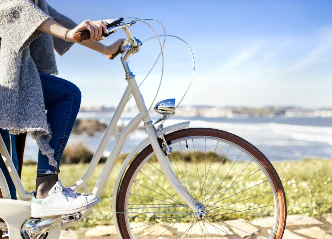 Una joven con su bicicleta y Gijón al fondo. 