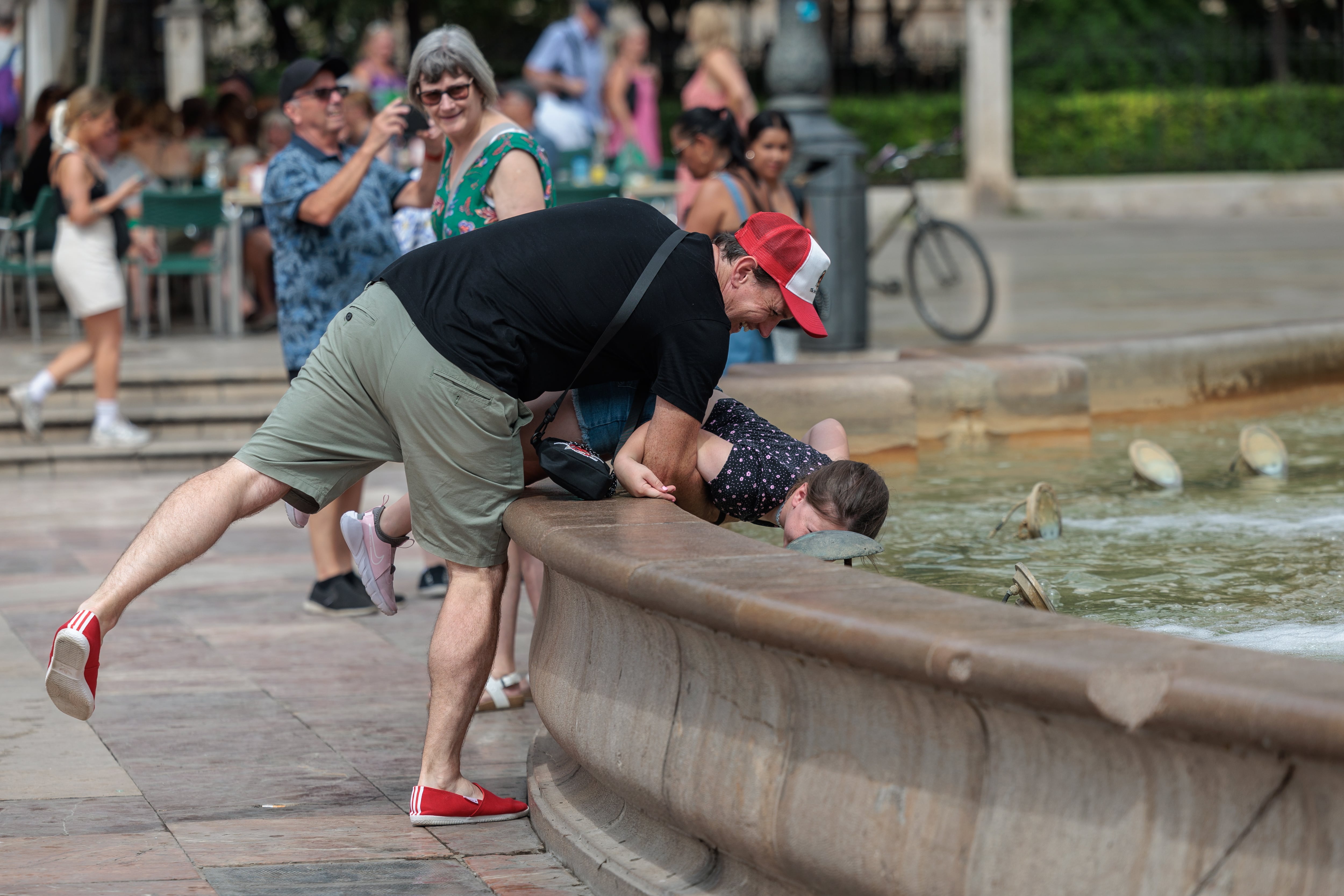 Un hombre refresca a su hijo en una fuente del centro de València