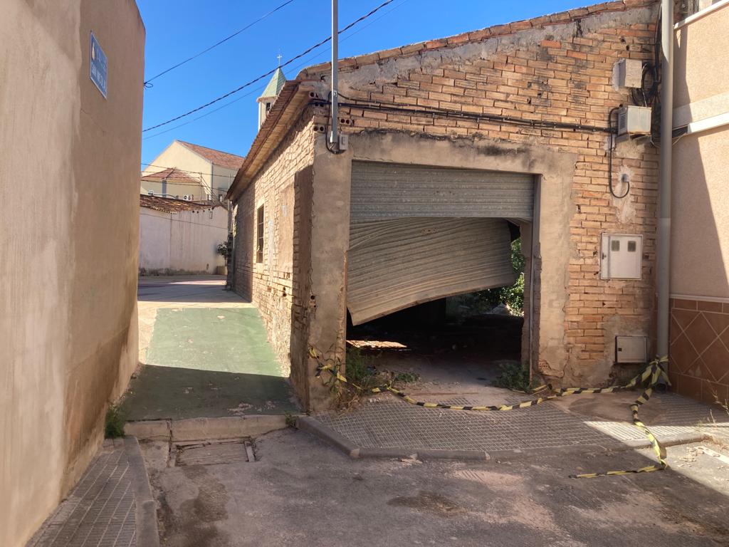 La nave de la antigua carpintería de la calle San Nicolás de Javalí Viejo, que hizo de tapón, permanece en el mismo estado en el que quedó hace un año. La persiana sigue en el mismo estado y todavía se puede ver la cita que precintaba su acceso