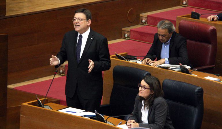 El president de la Generalitat Valenciana, Ximo Puig, respon una de les preguntes de la sessió de control. Imatge mitjana de Puig de peu al seu escó gesticulant i Mónica Oltra asseguda. Horitzontal. 29/10/2015.