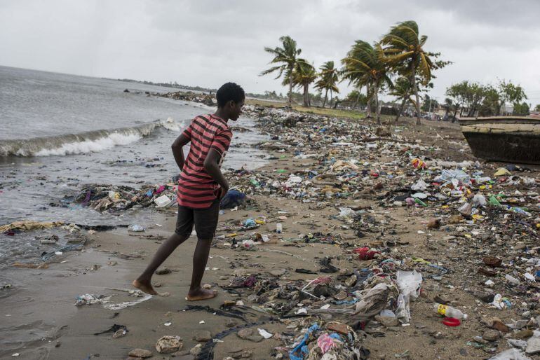 Un joven camina por una playa cubierta de desechos.