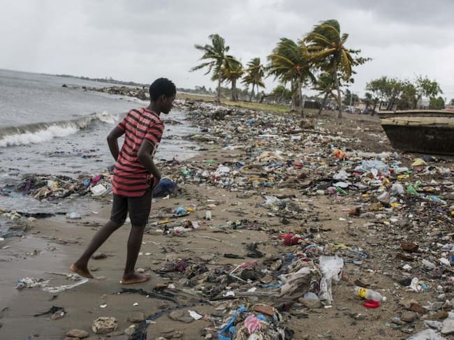 Un joven camina por una playa cubierta de desechos.