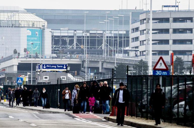 Vista de un edificio del aeropuerto con los cristales rotos (al fondo) mientras pasajeros y trabajadores evacúan el edificio de la terminal tras registrarse explosiones 