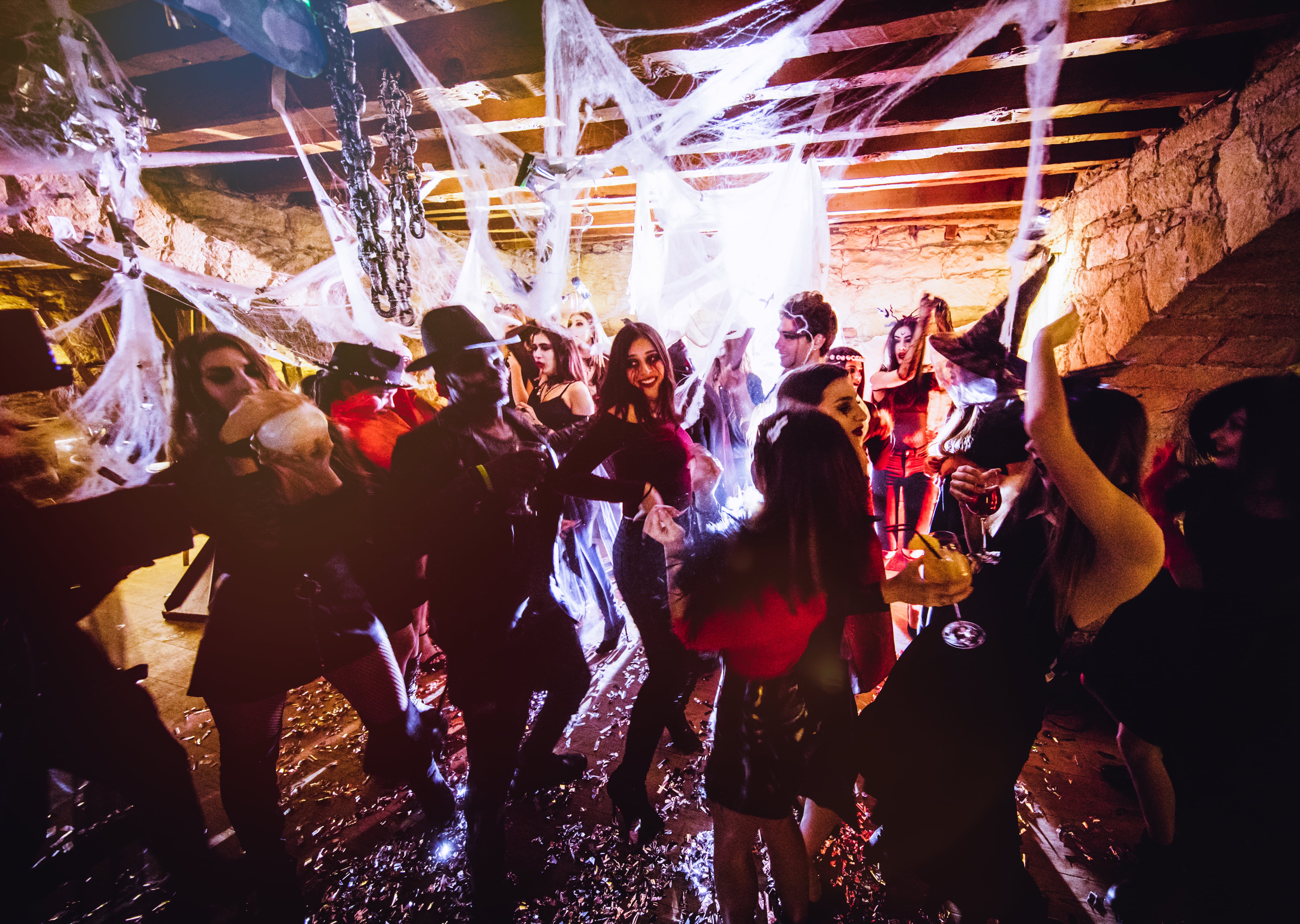 Young multi-ethnic friends dressed-up in Halloween costumes dancing and drinking at nightclub dungeon party