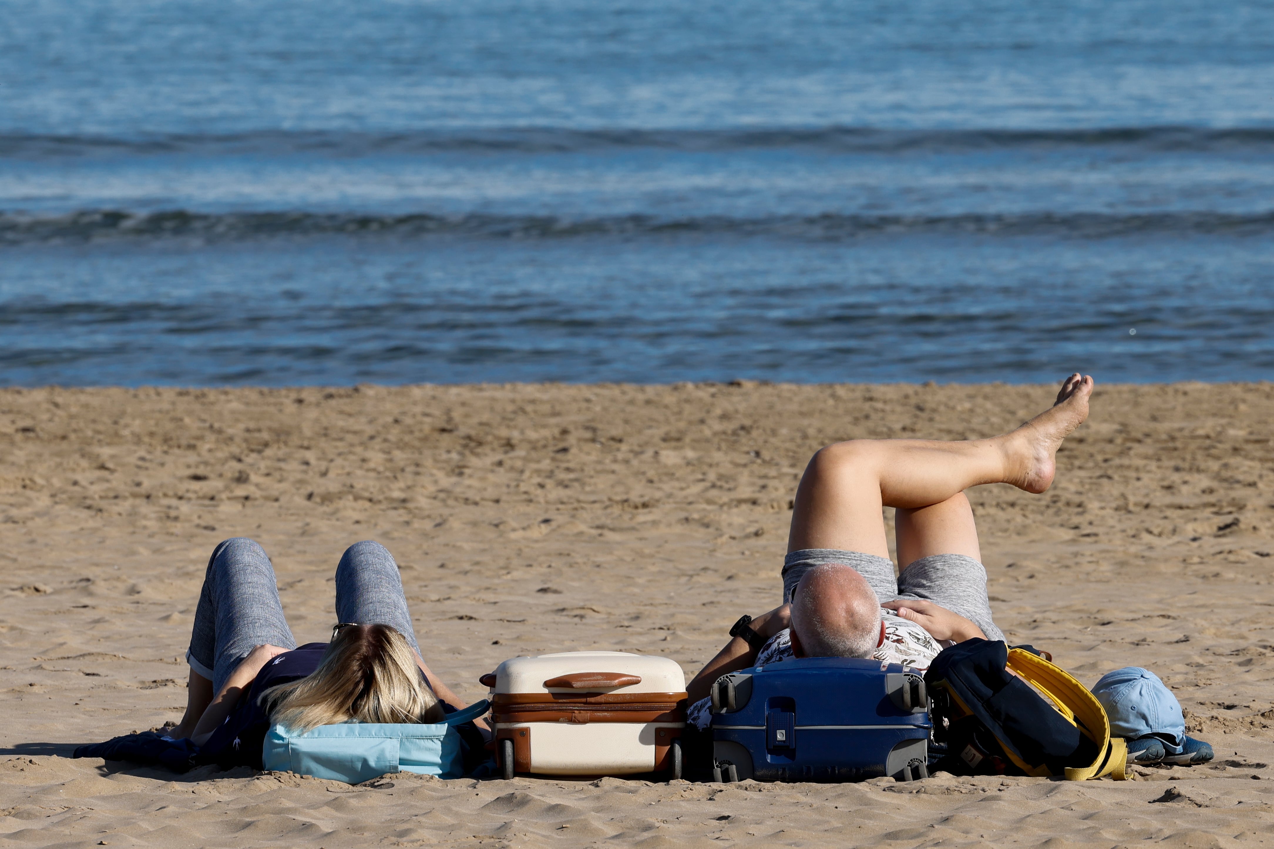 VALENCIA, 11/12/2023.- Dos turistas disfrutan de las buenas temperaturas junto a sus maletas en la playa de la Malvarrosa cuando la Agencia Estatal de Meteorología (Aemet) prevé para hoy lunes un aumento de las temperaturas mínimas en el interior del norte de Alicante y del sur de Castellón y de las máximas en el tercio sur de la Comunitat y que los termómetros lleguen o superen los 25 grados en Alicante y València en un &quot;nuevo episodio cálido&quot; sin &quot;precedentes a estas alturas del año&quot;. EFE/Ana Escobar
