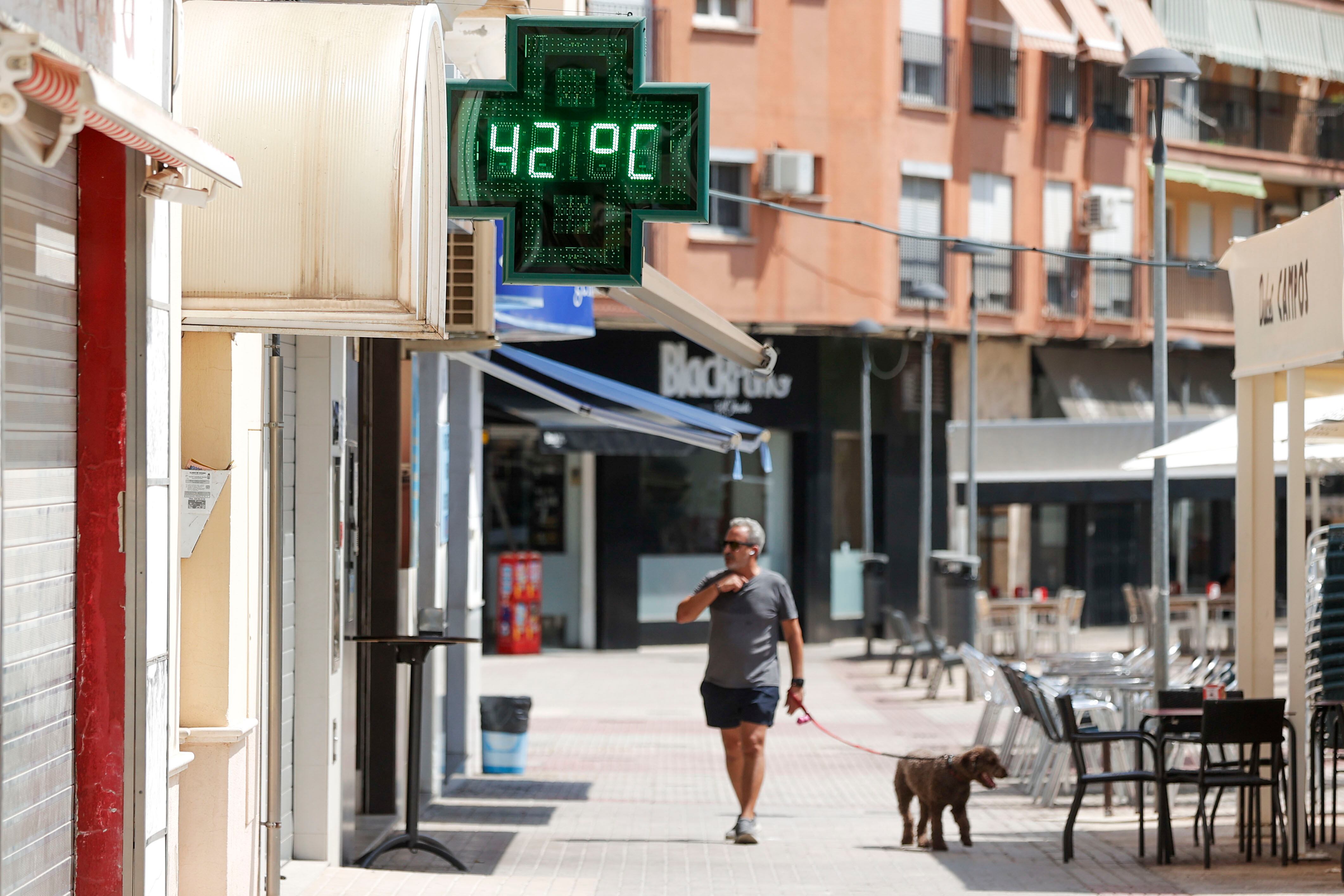 Un hombre pasea con su perro ante un termómetro urbano que marca una temperatura de 42º en la localidad valenciana de Xàtiva.