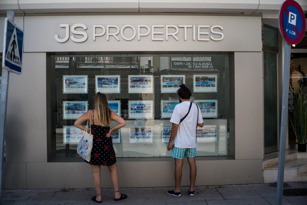 Dos personas observan inmuebles en alquiler y en venta en un escaparate de una inmobiliaria en Palma.