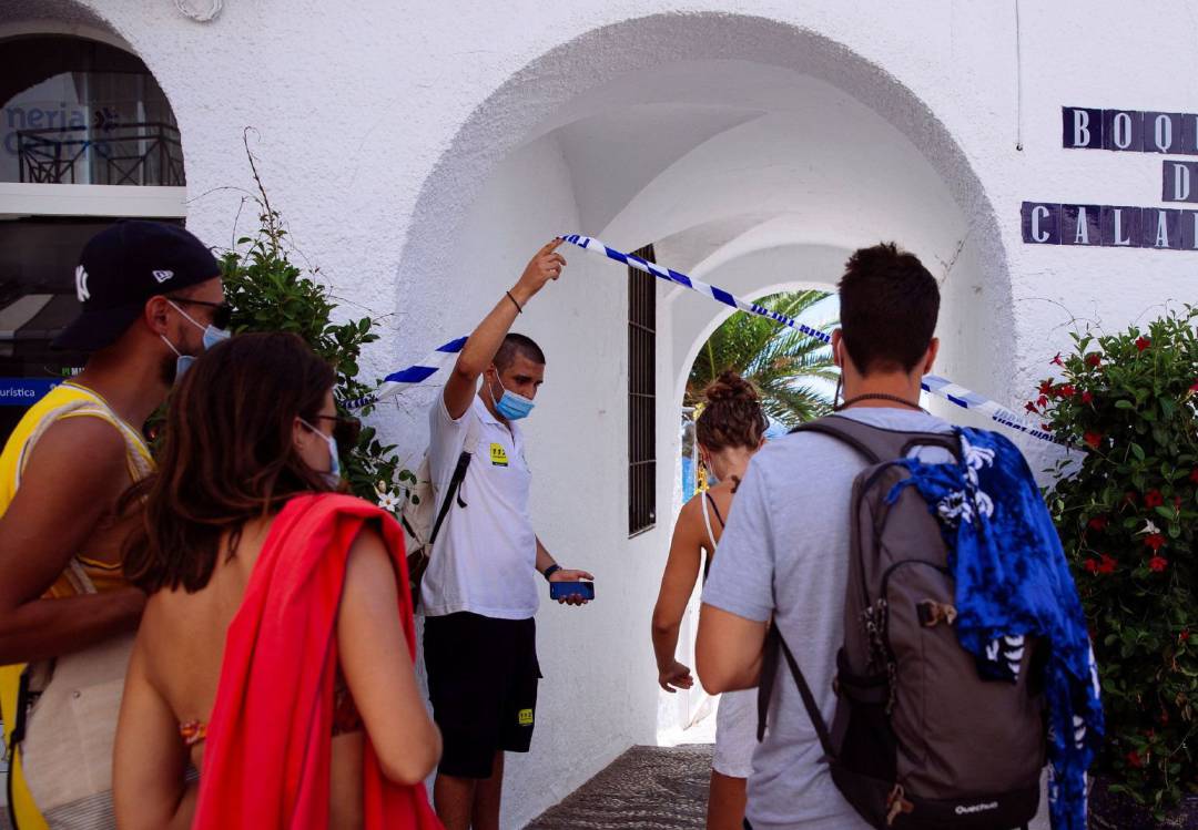 Un auxiliar de playa de la Junta de Andalucía (i), permite el acceso a bañistas a la playa de Papagayo en Nerja (Málaga)