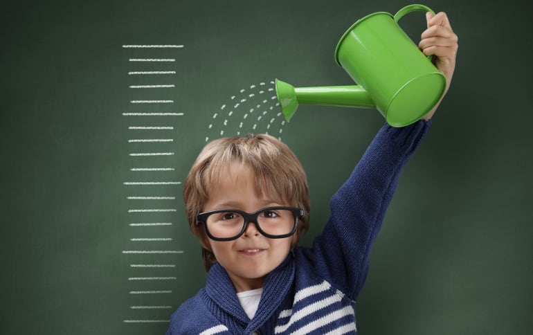 Imagen de un niño midiendo su estatura en una pared y simulando el crecimiendo echándose agua ficticia con una regadera.