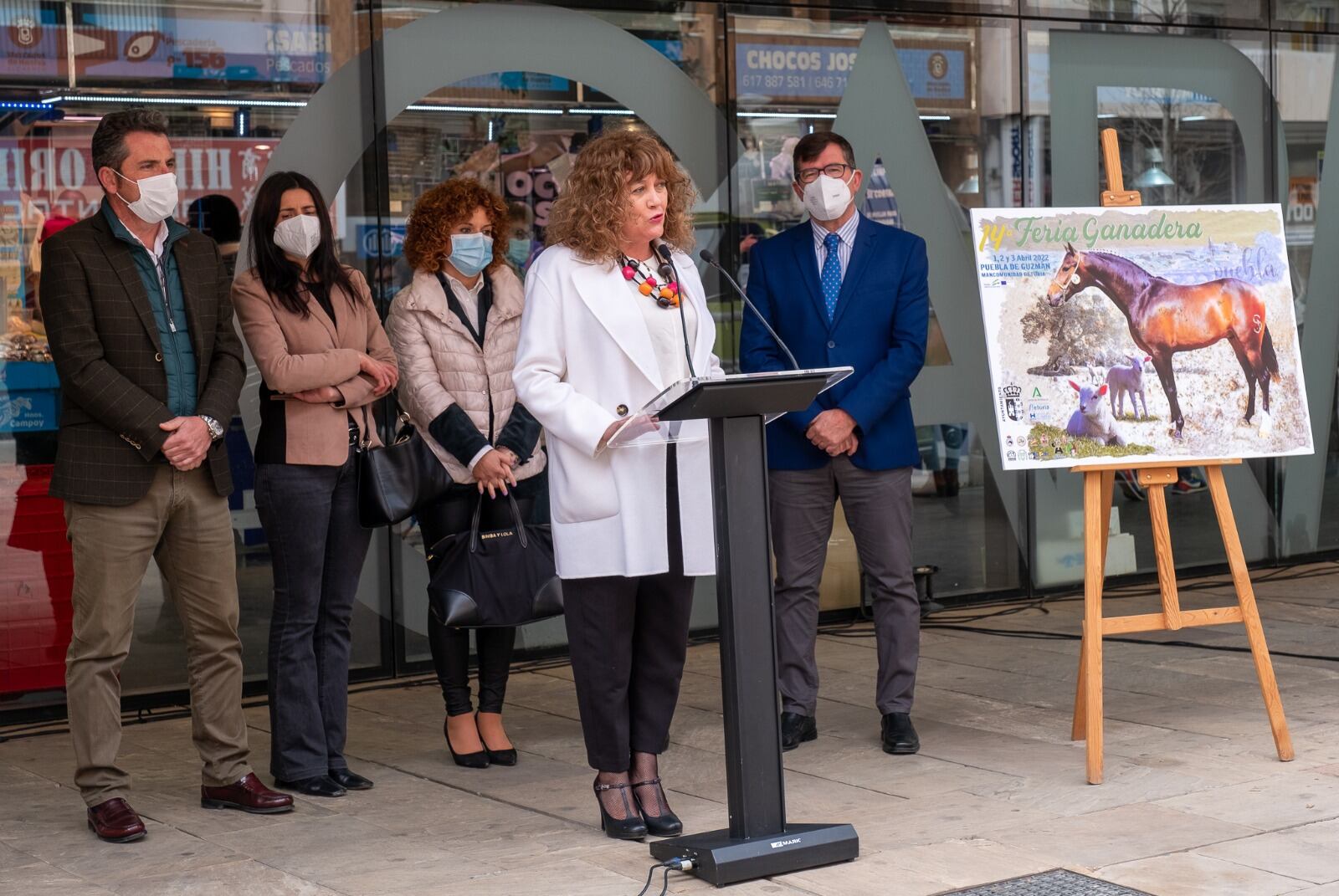 Dolores Ruiz, en el atril, durante la presentación de la Feria Ganadera de Puebla de Guzmán a las puertas del Mercado del Carmen, en Huelva. 