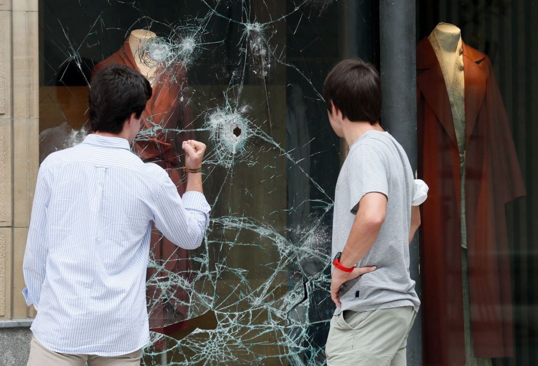 Dos jóvenes viendo los daños en el escaparate de un comercio del centro de la ciudad