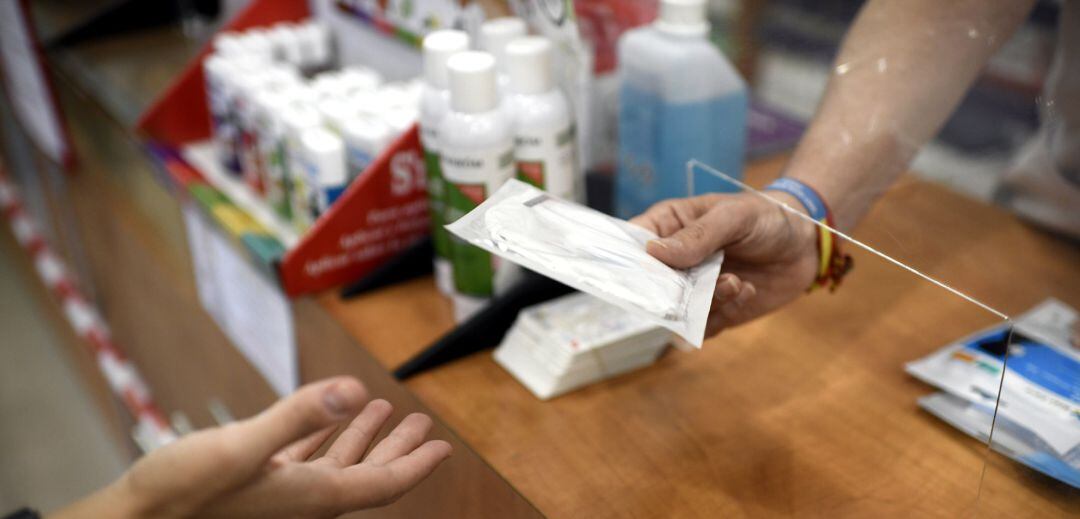 Un farmacéutico entrega a un cliente una mascarilla