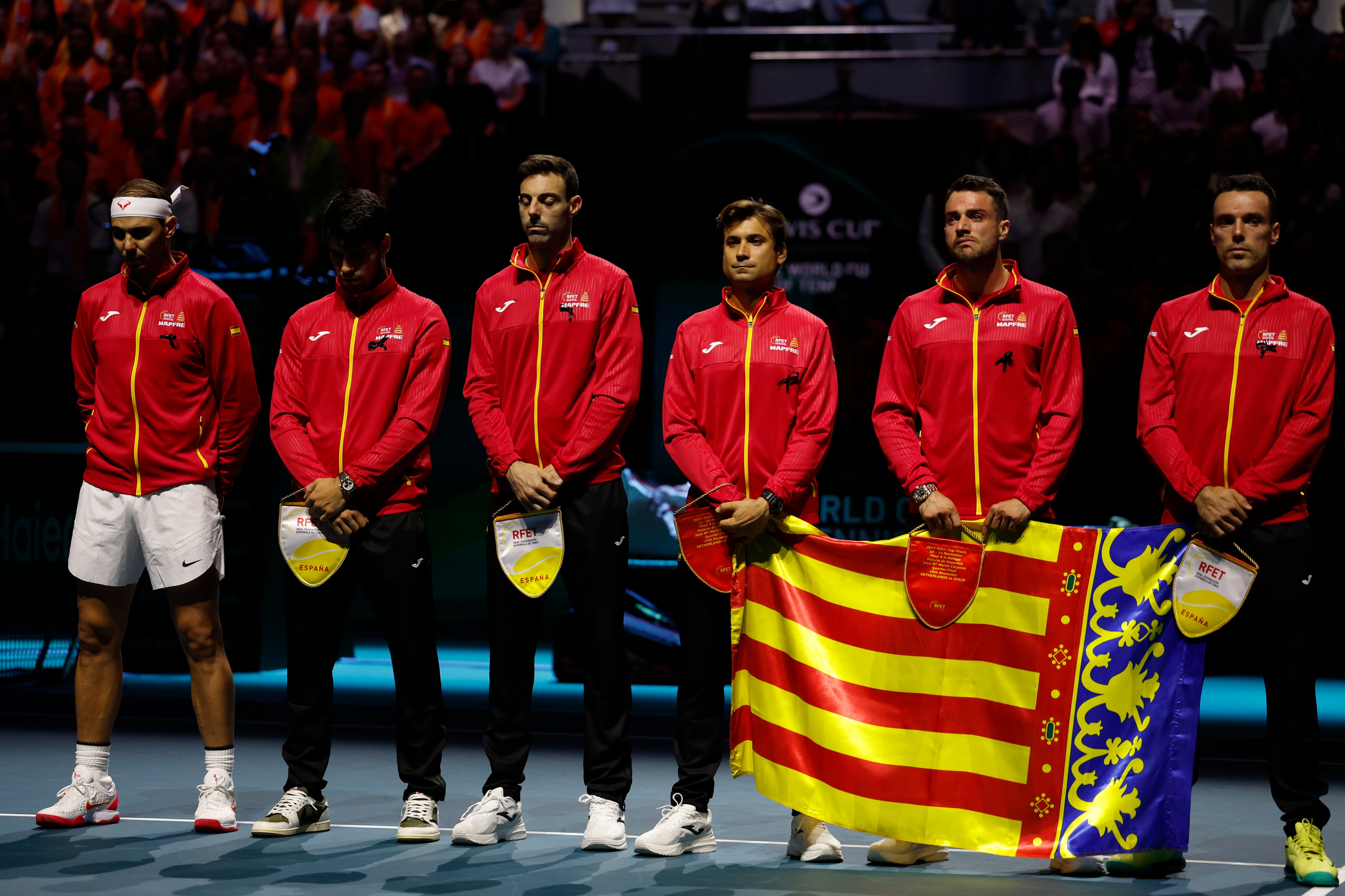 MÁLAGA, 19/11/2024.- Los tenistas Rafa Nadal (izda) y Carlos Alcaraz (2i), que junto al equipo español, capitaneado por David Ferrer (3d), con Roberto Bautista (dcha), Marcel Granollers (3i) y Pedro Martínez, y junto a la bandera de la Comunidad Valenciana han guardado un minuto de silencio en memoria a las víctimas de las inundaciones en Valencia, momentos antes de comenzar las Finales de la Copa Davis que abren los equipos de España y Países Bajos, este martes en Málaga en el Palacio de los Deportes José María Martín Carpena. EFE/Jorge Zapata
