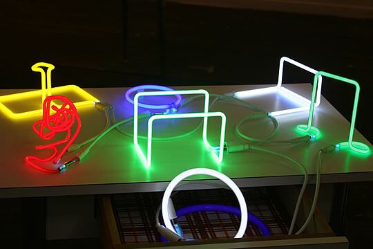 Instalación de pequeños artilúgios de neón sobre una mesa.