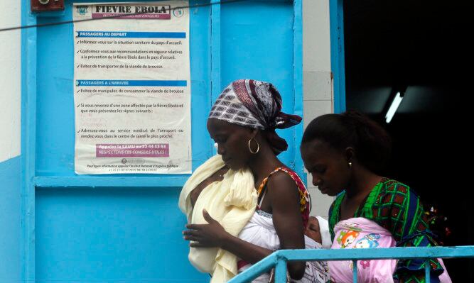 Mujeres a las puertas de un hospital de maternidad junto a un cartel preventivo contra el ébola