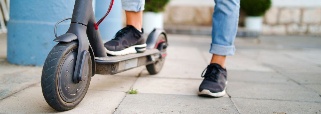 Persona parada en una acera con un patinete eléctrico. Foto de recurso