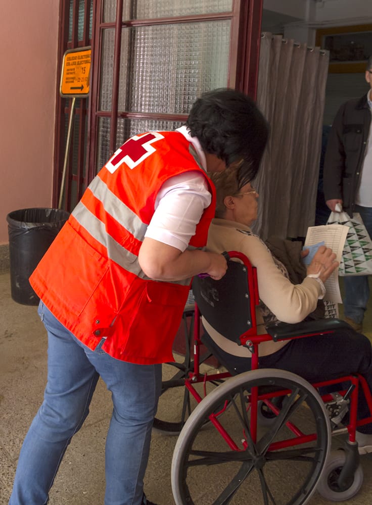 Voluntaria de Cruz Roja ayudando a una persona a acudir al colegio electoral