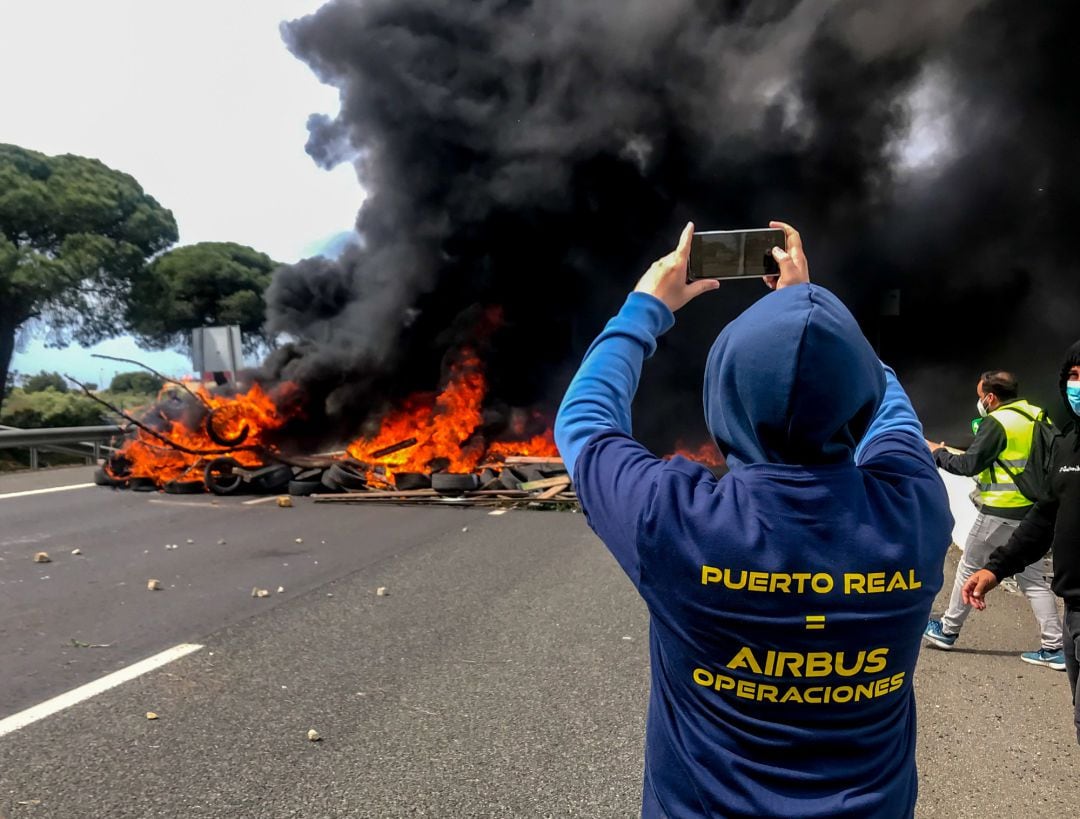 Un trabajador fotografía el incendio provocado por parte de la plantilla de la factoría de Airbus de Puerto Real en la autovía CA- 35 que da acceso a los puentes de la Bahía de Cádiz,  como protesta por el cierre de la planta. Puerto Real (Cádiz) a 14 de 