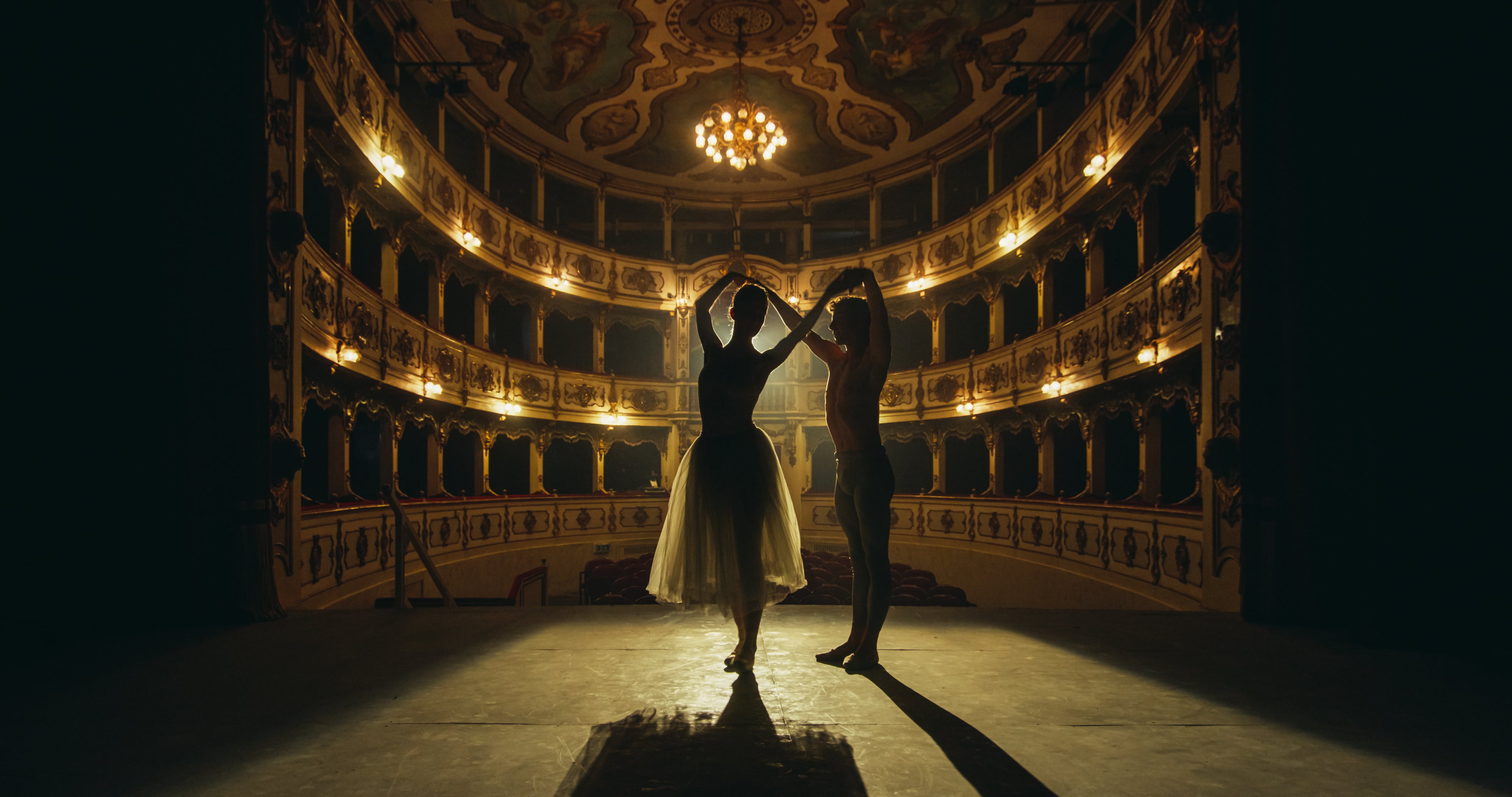 Cinematic shot of Young Couple of Classical Ballet Dancers Performing on the Stage of Classic Theatre with Dramatic Lighting. Male and Female Dancers Rehearse their Performance Together Before a show