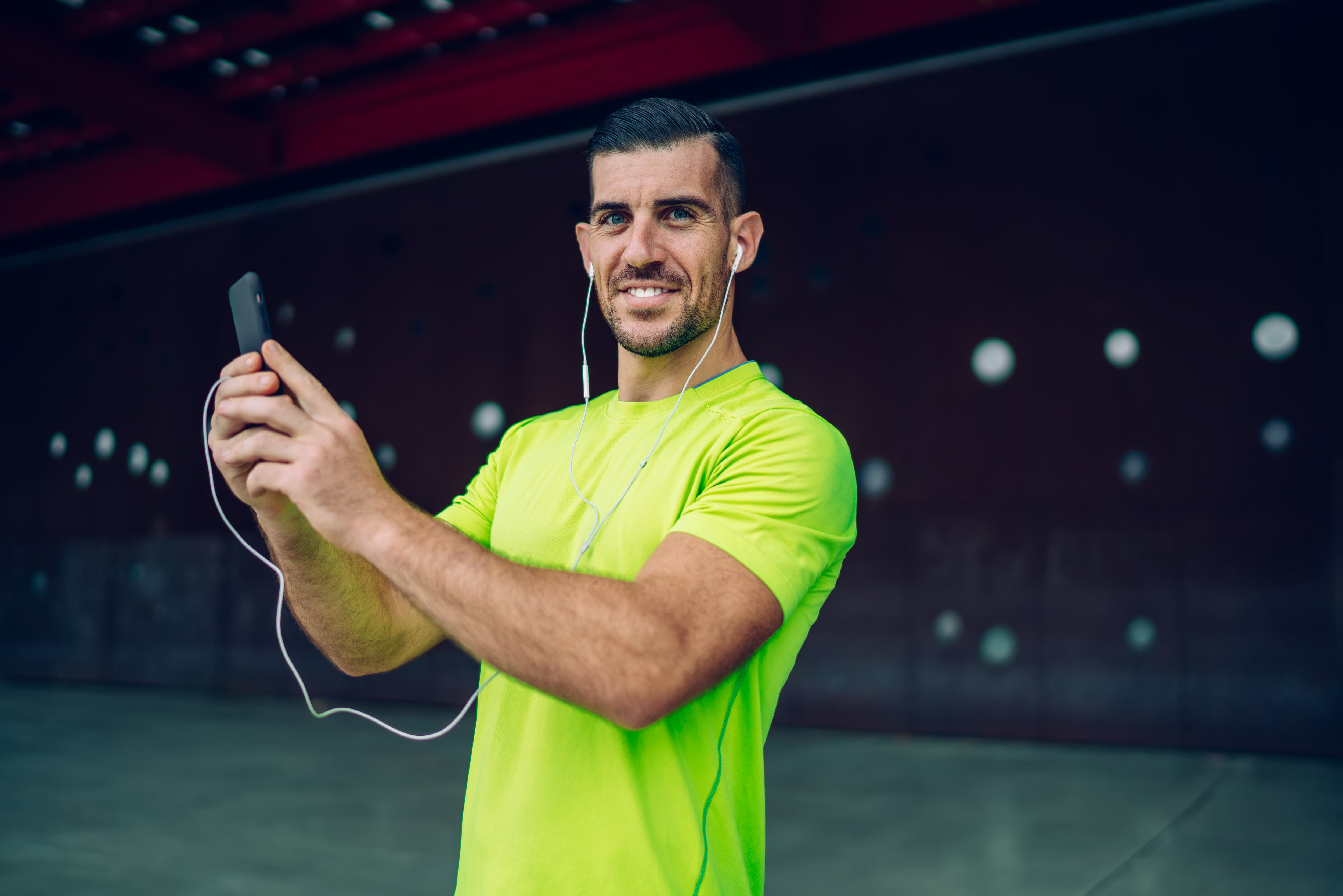 Happy sportive blogger shooting video vlog for sharing workout advices to social network using 4g wireless connection on smartphone device ,half length portrait of successful athlete in earphones