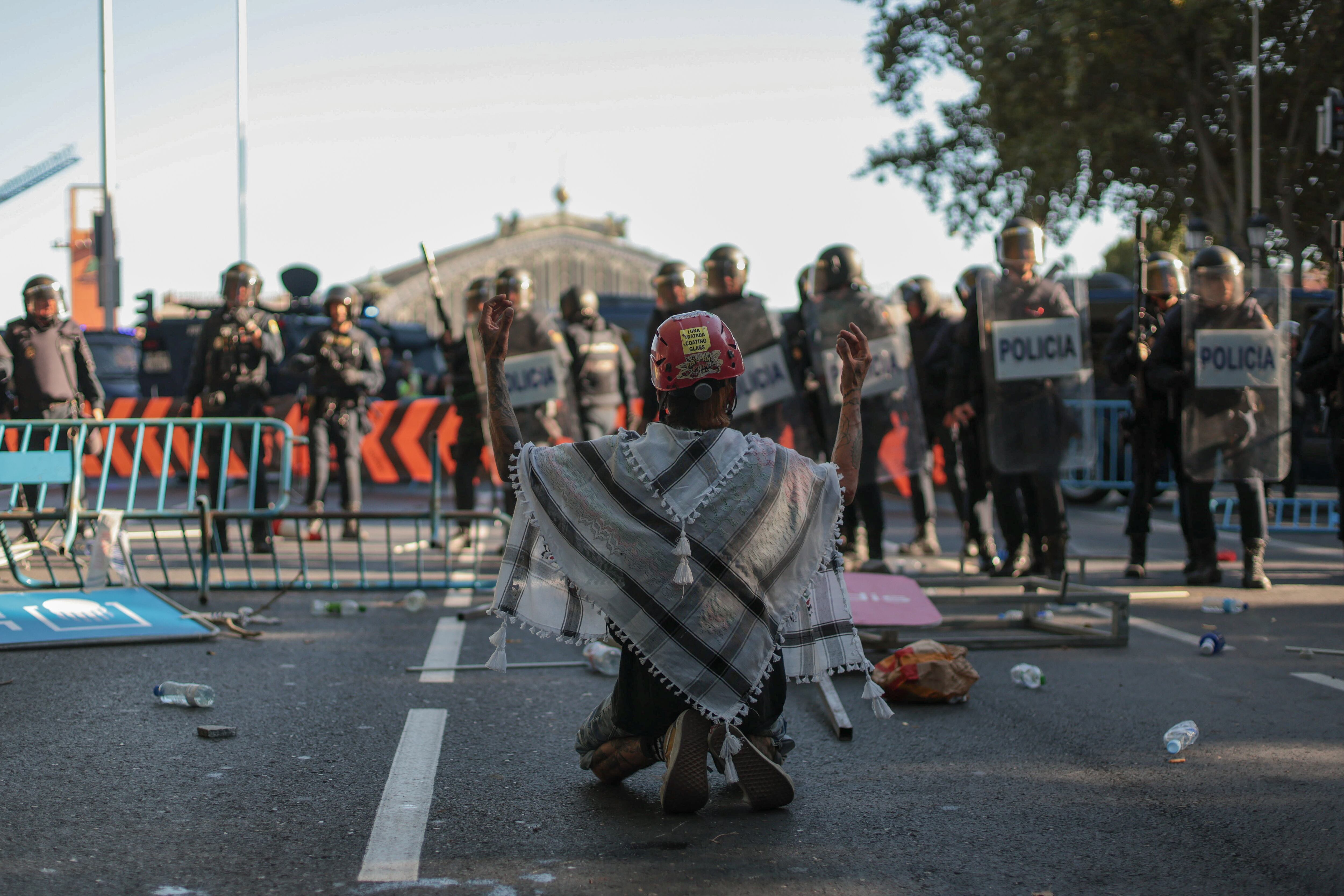 Un manifestante se arrodilla frente a las autoridades en la zona del paseo del Prado, en Madrid, durante la última etapa de La Vuelta