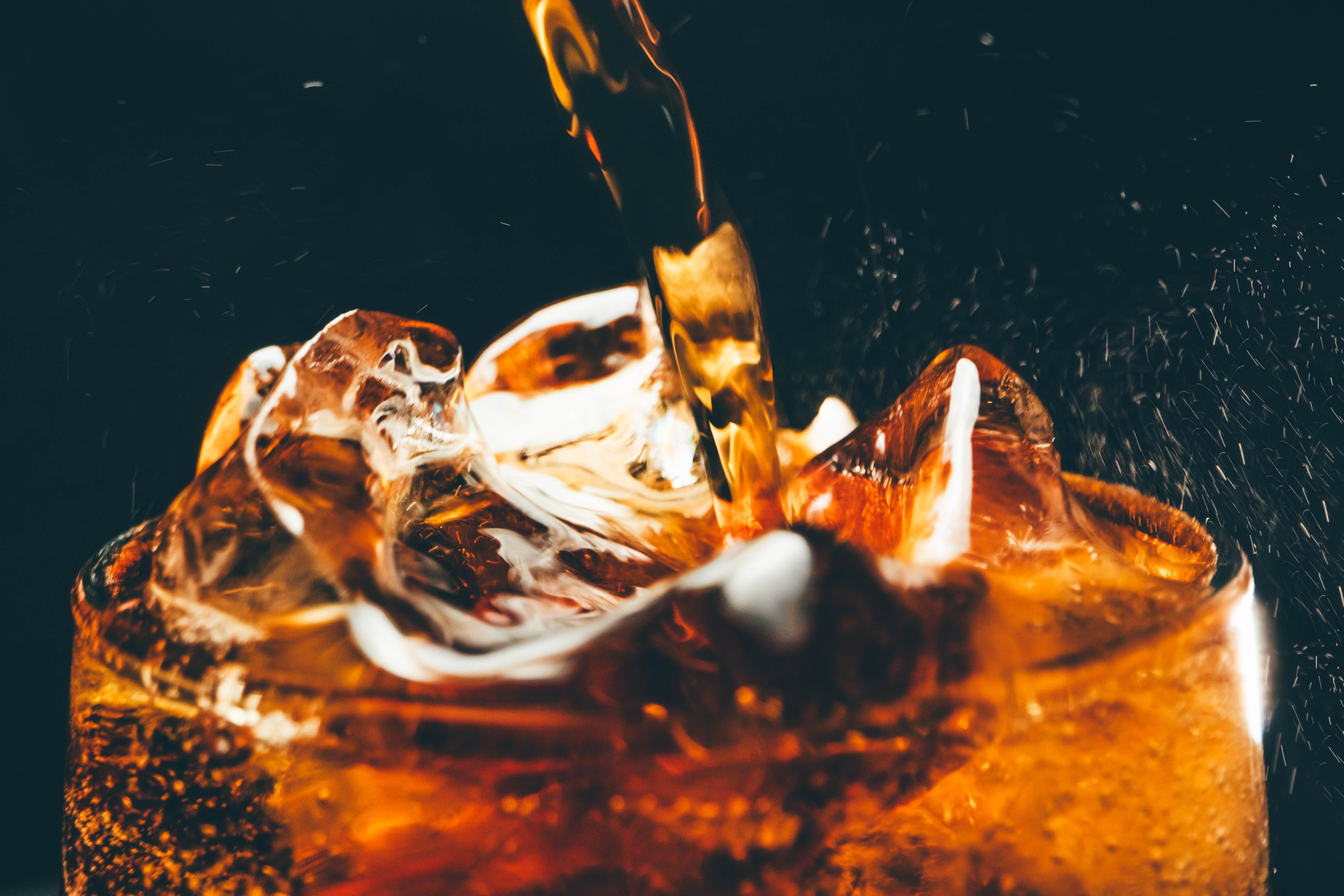 Una persona vierte un refresco sobre un vaso con hielos.