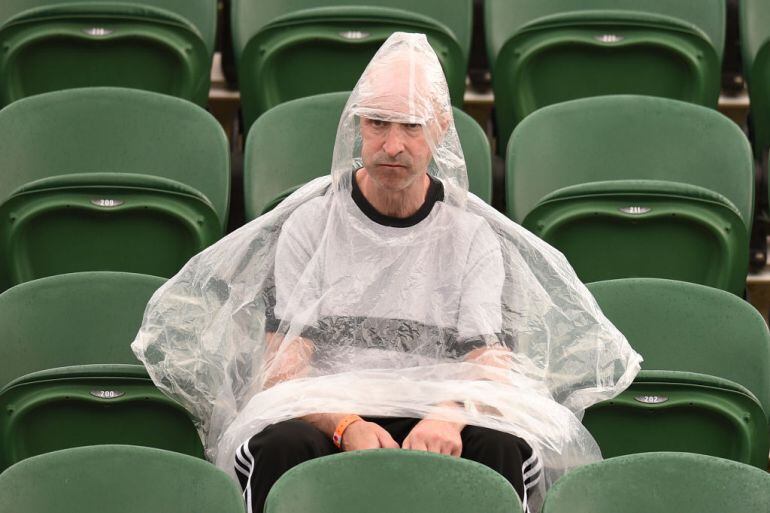 Un aficionado se protege de la lluvia durante un partido de tenis