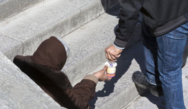 Una persona pide a los transeúntes, sentada en una escaleras