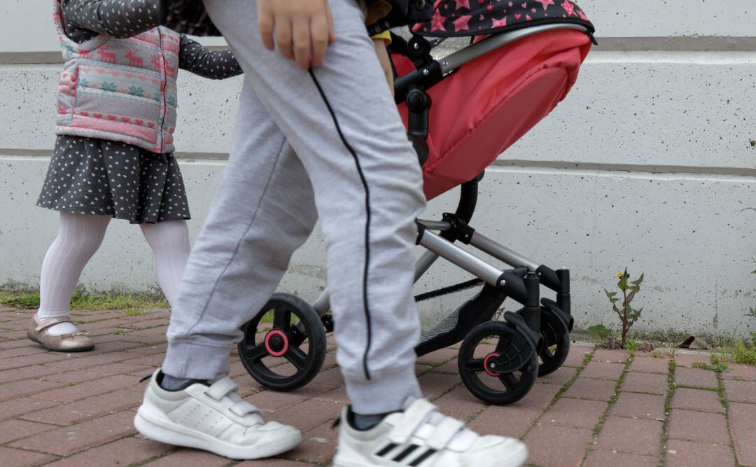 Una niña pasea por la calle empujando un carrito con un bebé de juguete junto a su padre y su hermano