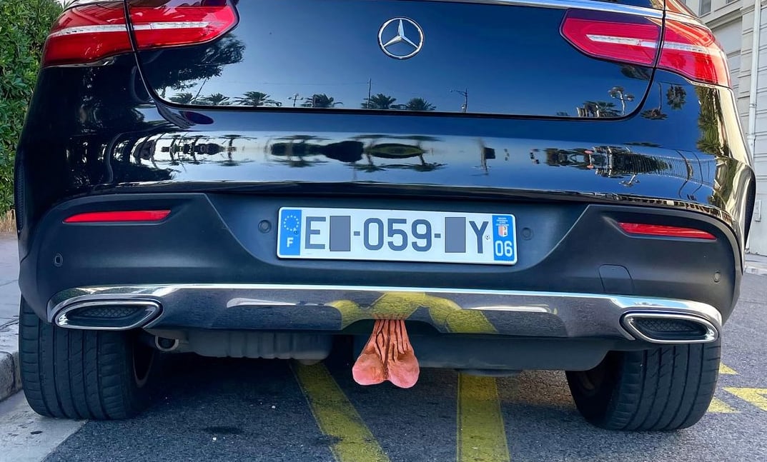 Los testículos de arcilla cuelgan del parachoques trasero del coche.