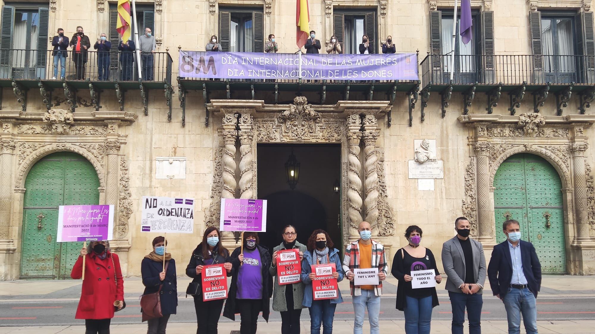 El bipartito en el balcón del Ayuntamiento de Alicante tras colocar la pancarta del 8M mientras que en la plaza protesta la oposición por la ordenanza de convivencia cívica