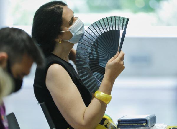 Una mujer con mascarilla se abanica